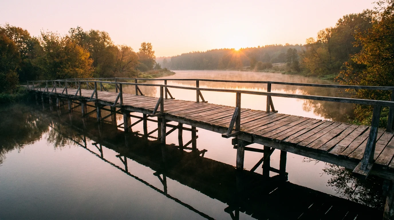 A quiet sunrise over a small wooden bridge and calm river.